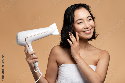 Nice-looking cute lady drying healthy hair isolated on beige studio background