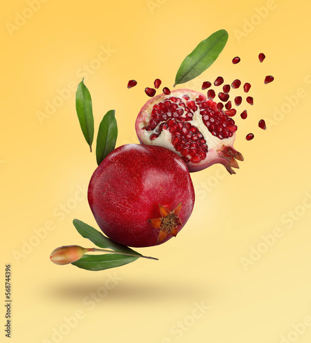 Delicious ripe pomegranate fruits and leaves falling on color background