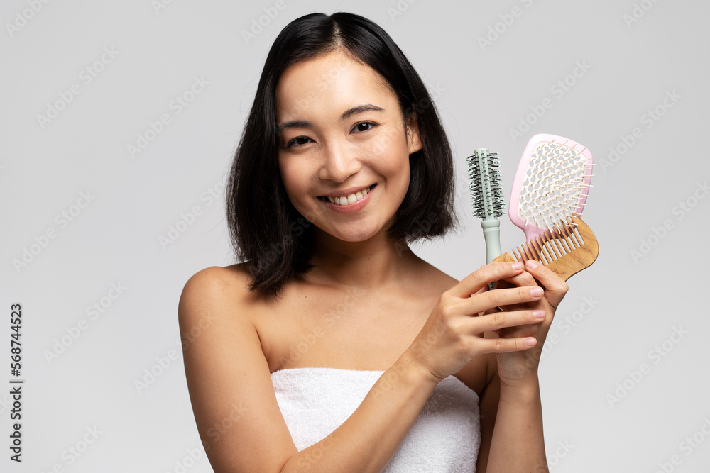 Smiling woman preparing brushing hair with comb while posing at studio over white wall Smiling woman preparing brushing hair with comb while posing at studio over white wall