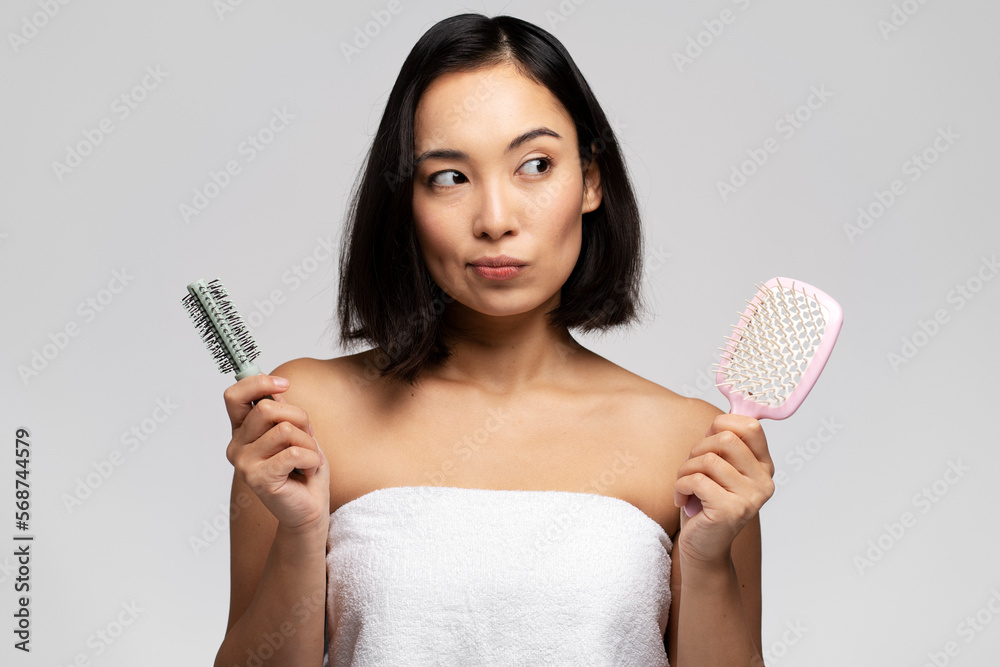 Pensive woman pondering with two hair combs while posing Pensive woman pondering with two hair combs while posing