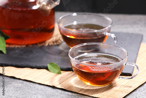Aromatic hot tea in glass cups and teapot on light grey table, closeup