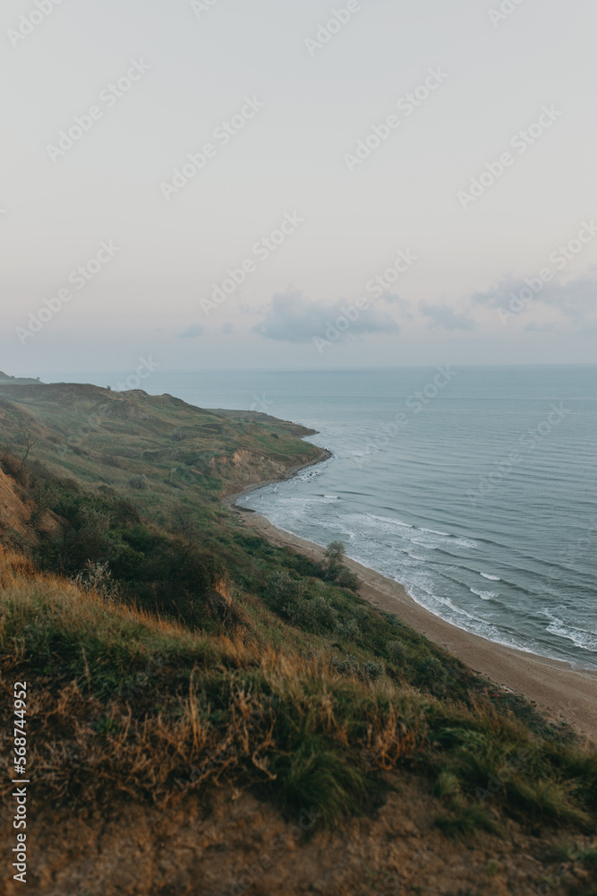 Outdoor image of picturesque autumn view of wild sea bay on cloudy rainy day, blue water with small waves touching edge of green hills. Traveling and adventures, hiking on seacoast