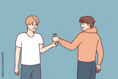 Two young guys bump their fists when they meet, making greeting to members of student fraternity. Positive teenage boys in casual clothes say goodbye after fun together walk