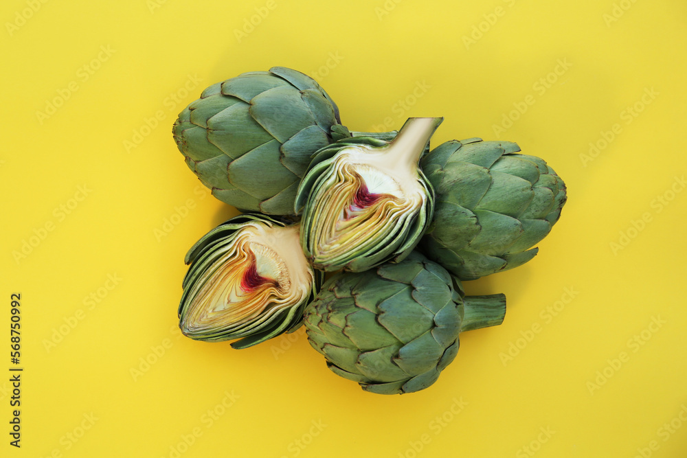 Fototapeta premium Cut and whole fresh raw artichokes on yellow background, flat lay