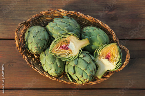 Wicker basket with fresh raw artichokes on wooden table, top view photo