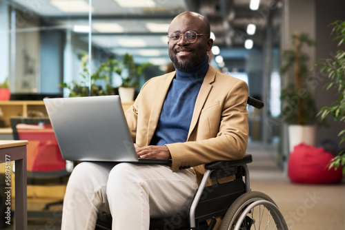 Fotomurale Happy young black man with disability sitting in wheelchair in office and lookin