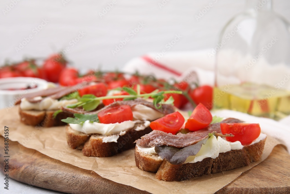 Delicious bruschettas with anchovies, tomatoes, microgreens and cream cheese on white table, closeup Delicious bruschettas with anchovies, tomatoes, microgreens and cream cheese on white table, closeup