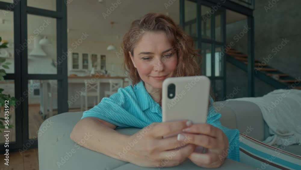 lady with red curly hair using mobile phone at home chatting online with happy smiling sitting on sofa in living room at home technology for communication
