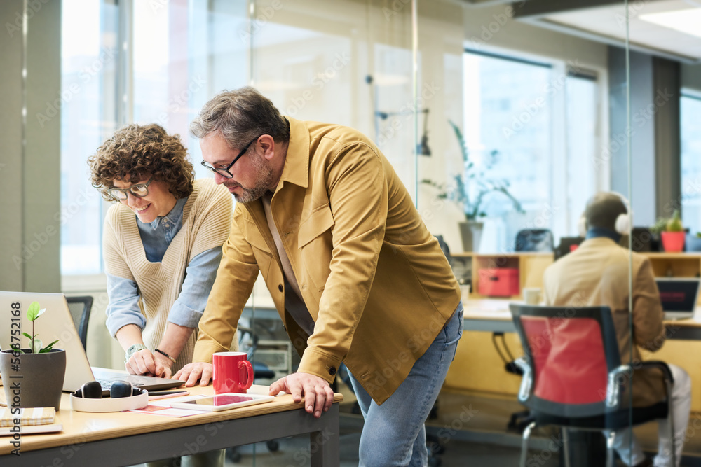 Two colleagues in casualwear watching online video representing information for their new business project by workplace Two colleagues in casualwear watching online video representing information for their new business project by workplace