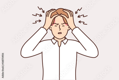 Tormented man clutches head and squints due to overworking and large number of work tasks