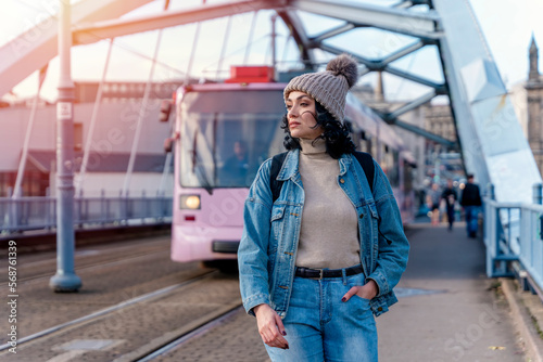 a young woman in a denim jacket is talking on the phone and waiting for a tram, bus at the stop Lifestyle photo