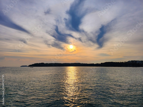 Orange sun and blue sky with clouds at sunset reflected in the sea water