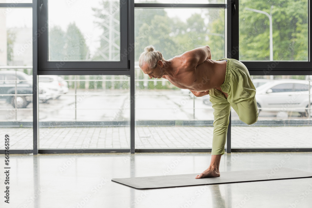 Foto de shirtless and barefoot man doing half bound lotus tree pose in