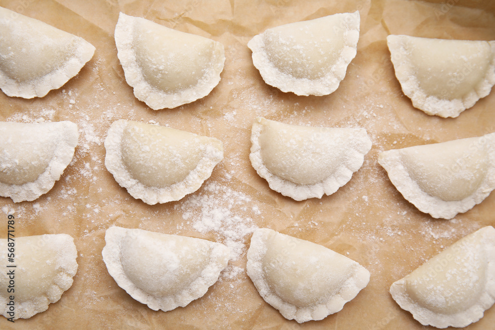 Raw dumplings (varenyky) with tasty filling and flour on parchment paper, flat lay