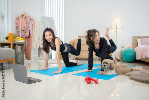 Two beautiful Asian girls wearing workout clothes and smiling with dogs in bedroom. woman on exercise mat with dumbbells and tablet