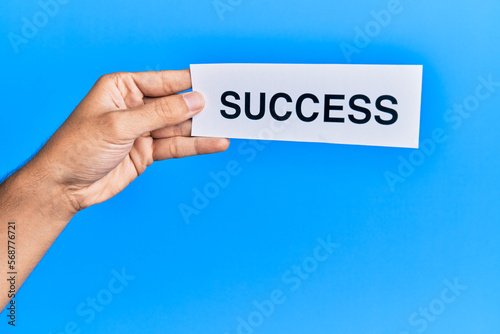 Hand of caucasian man holding paper with success word over isolated blue background