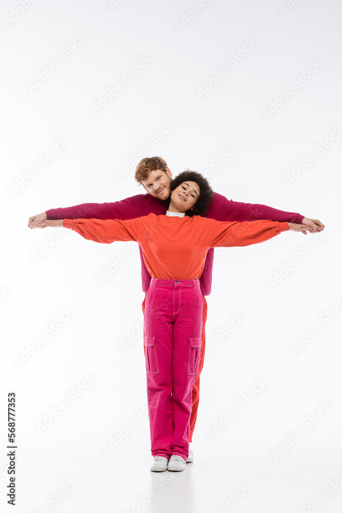 happy and interracial couple in magenta color clothes showing t letter on white background. happy and interracial couple in magenta color clothes showing t letter on white background.