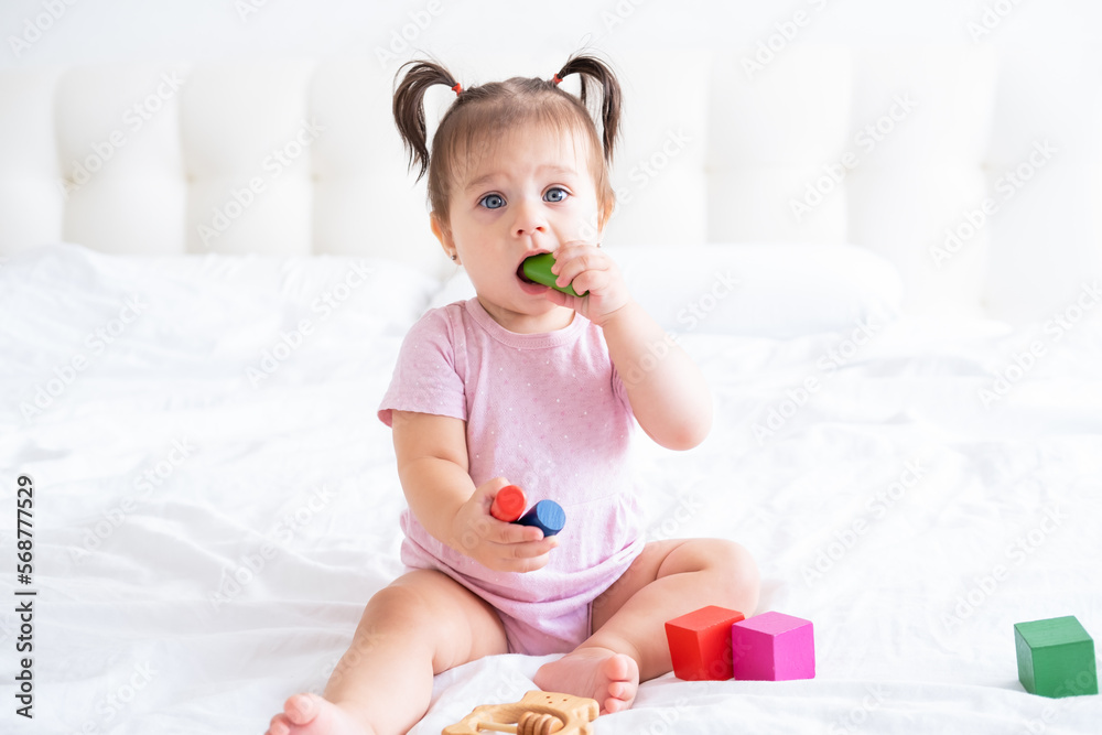 funny baby girl in pink bodysuit playing with children wooden cubes toys on bed funny baby girl in pink bodysuit playing with children wooden cubes toys on bed