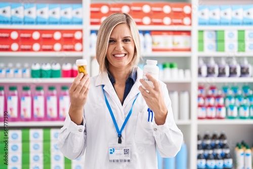 Young blonde woman pharmacist smiling confident holding pills bottles at pharmacy