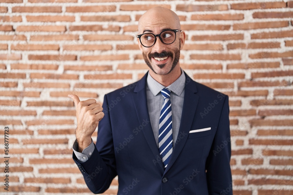 Bald man with beard wearing business clothes and glasses smiling with happy face looking and pointing to the side with thumb up. Bald man with beard wearing business clothes and glasses smiling with happy face looking and pointing to the side with thumb up.