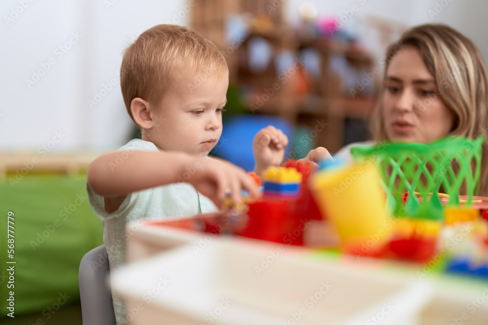 Teacher and toddler playing with construction blocks sitting on table at kindergarten Teacher and toddler playing with construction blocks sitting on table at kindergarten