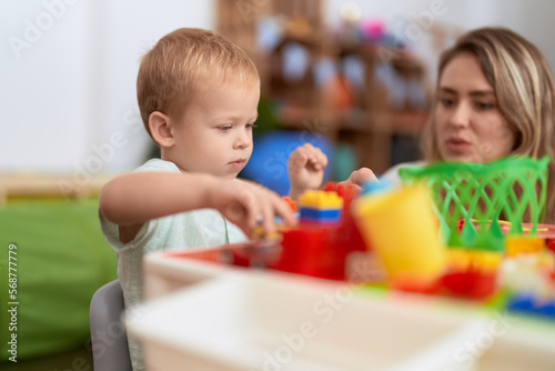 Teacher and toddler playing with construction blocks sitting on table at kindergarten