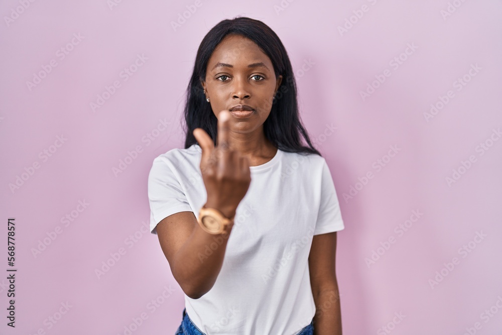 African young woman wearing casual white t shirt showing middle finger, impolite and rude fuck off expression African young woman wearing casual white t shirt showing middle finger, impolite and rude fuck off expression