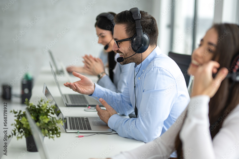 Side view portrait of handsome male IT support executive agent talking to customer while working in call center. Side view portrait of handsome male IT support executive agent talking to customer while working in call center.