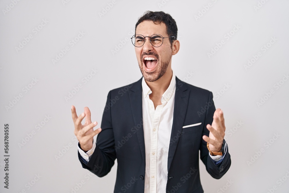 Handsome business hispanic man standing over white background crazy and mad shouting and yelling with aggressive expression and arms raised. frustration concept. Handsome business hispanic man standing over white background crazy and mad shouting and yelling with aggressive expression and arms raised. frustration concept.