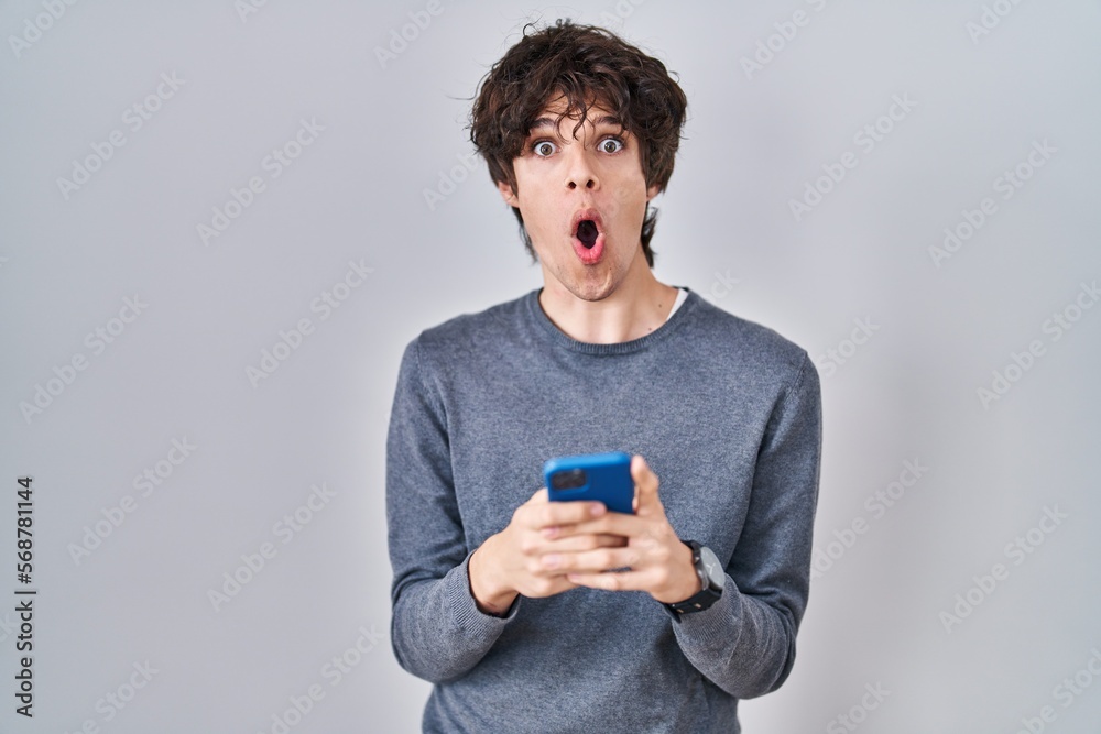 Young man using smartphone typing a message afraid and shocked with surprise and amazed expression, fear and excited face. Young man using smartphone typing a message afraid and shocked with surprise and amazed expression, fear and excited face.
