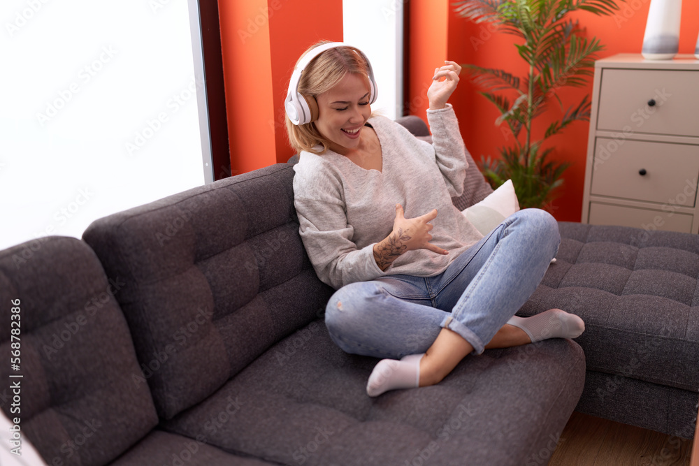 Young blonde woman listening to music doing guitar gesture at home