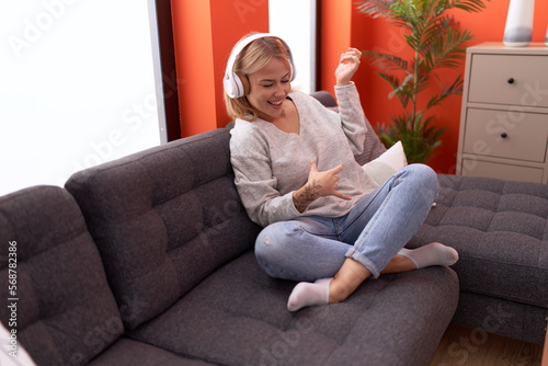 Young blonde woman listening to music doing guitar gesture at home