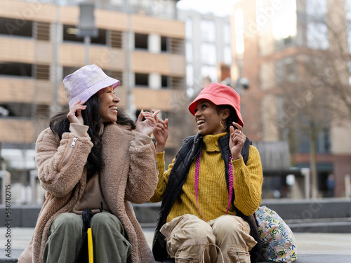 Two young women in urban setting, trying on hats