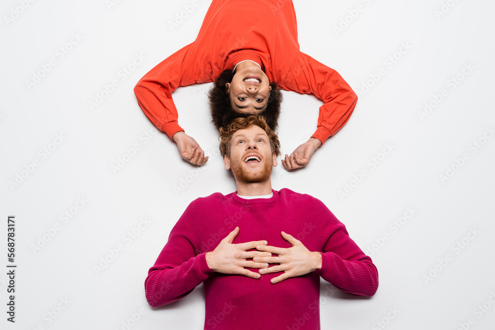 top view of happy redhead man in magenta color clothes and excited african american woman lying on white. top view of happy redhead man in magenta color clothes and excited african american woman lying on white.