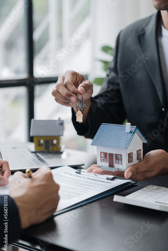 Real estate agents, insurance sales agents, and young Asian businessmen handing home keys and model homes to homebuyers after signing sales contracts are satisfied in the office. photo