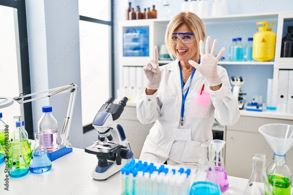 Middle age blonde woman working at scientist laboratory showing and pointing up with fingers number six while smiling confident and happy. Middle age blonde woman working at scientist laboratory showing and pointing up with fingers number six while smiling confident and happy.
