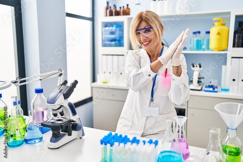 Middle age blonde woman working at scientist laboratory clapping and applauding happy and joyful  smiling proud hands together