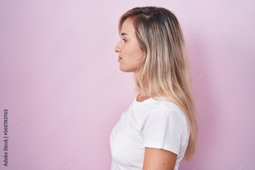 Young blonde woman standing over pink background looking to side, relax profile pose with natural face and confident smile. Young blonde woman standing over pink background looking to side, relax profile pose with natural face and confident smile.