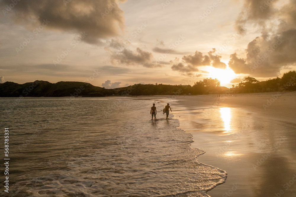 Indonesia, Lombok, Silhouette of surfers walking on beach at sunset