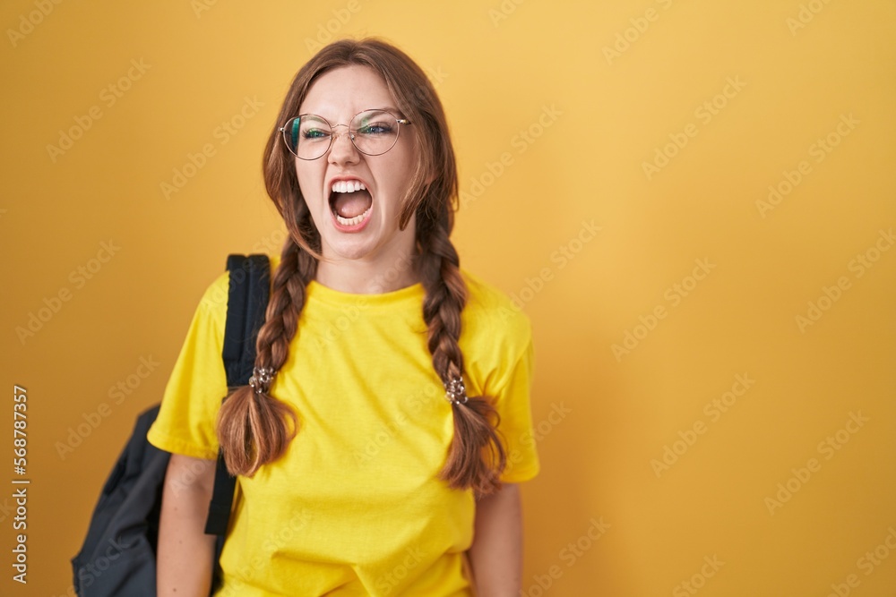 Young caucasian woman wearing student backpack over yellow background angry and mad screaming frustrated and furious, shouting with anger. rage and aggressive concept. Young caucasian woman wearing student backpack over yellow background angry and mad screaming frustrated and furious, shouting with anger. rage and aggressive concept.