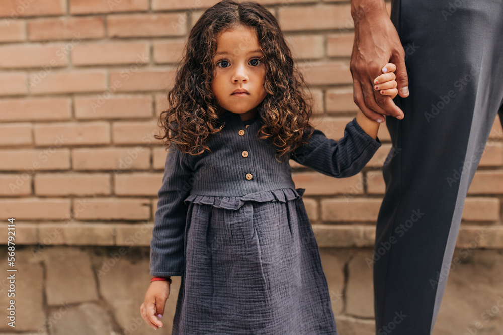 Adorable little girl looking at the camera while holding her father's hand Adorable little girl looking at the camera while holding her father's hand