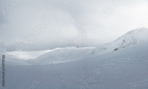Mountain landscape of a snowy valley without people, sunlight breaks through a foggy cloud