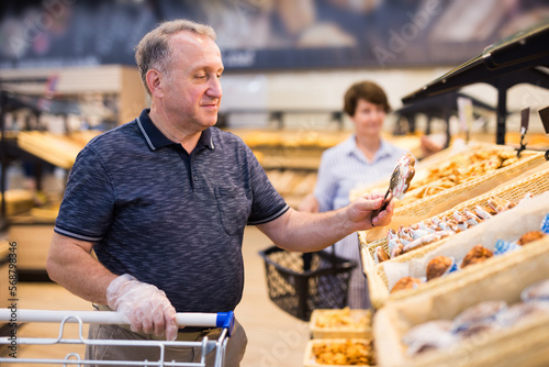 elderly retired man buying bread and pastries in grocery section of the supermarket