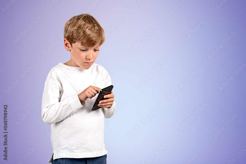 Serious handsome kid in casual wear standing holding smartphone Serious handsome kid in casual wear standing holding smartphone
