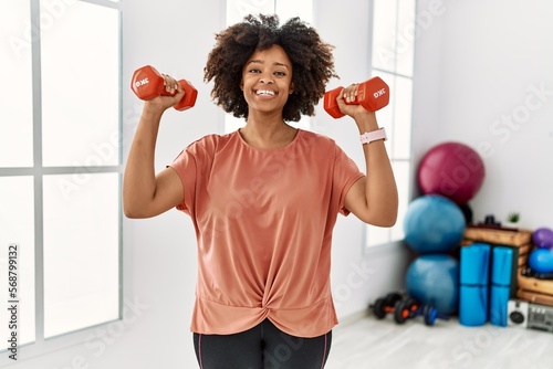 Young african american woman smiling confident training using dumbbells at sport center