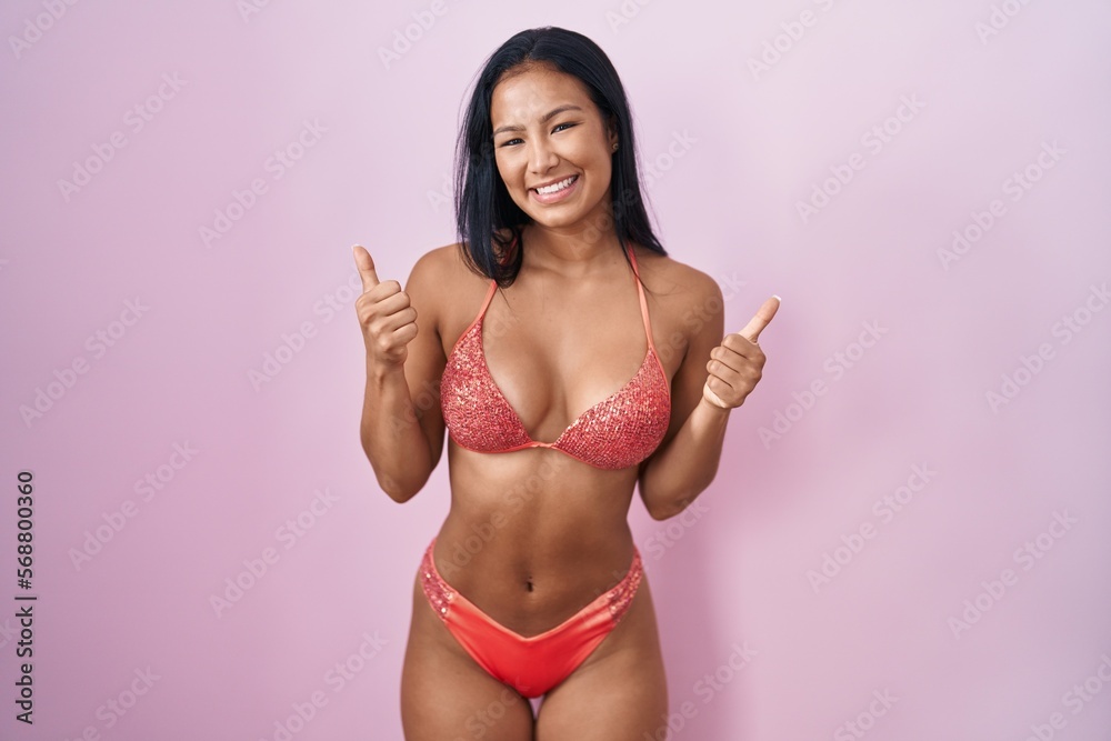 Hispanic woman wearing bikini success sign doing positive gesture with hand, thumbs up smiling and happy. cheerful expression and winner gesture. Hispanic woman wearing bikini success sign doing positive gesture with hand, thumbs up smiling and happy. cheerful expression and winner gesture.