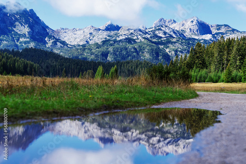 Panoramic view of the mountain peaks on a sunny summer day. The mountain range is reflected in puddles. Blue sky with clouds. © makedonski2015