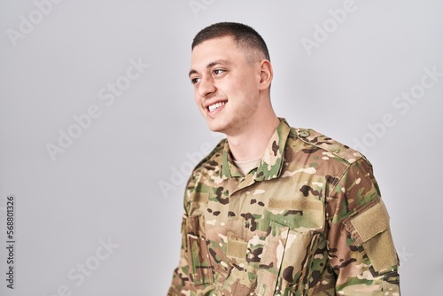 Young man wearing camouflage army uniform looking away to side with smile on face, natural expression. laughing confident.