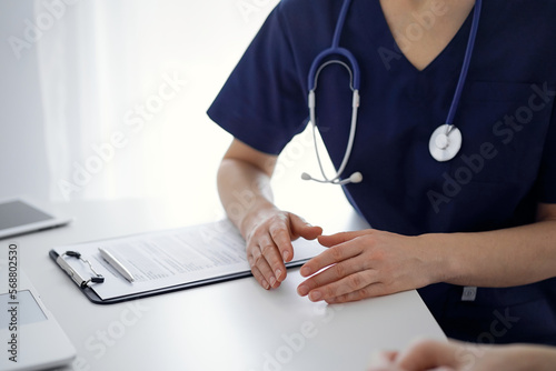 Doctor and patient sitting at the table in clinic while discussing something. The focus is on female physician's hands, close up. Medicine concept photo