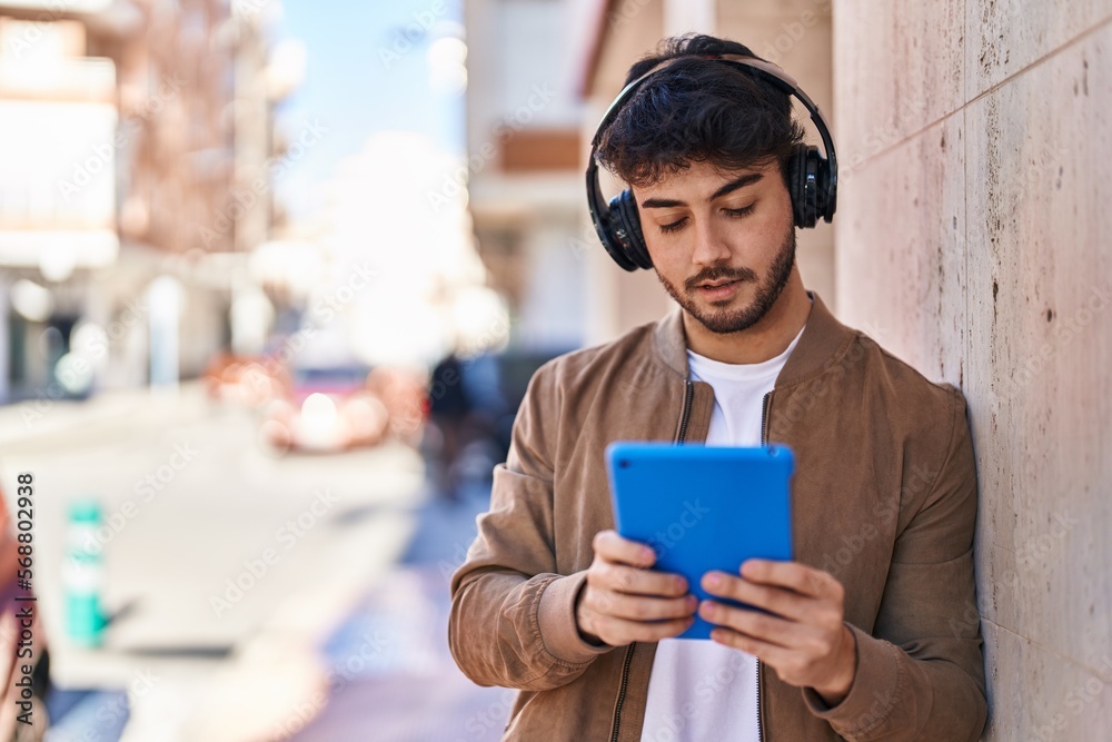 Young hispanic man using touchpad and headphones at street